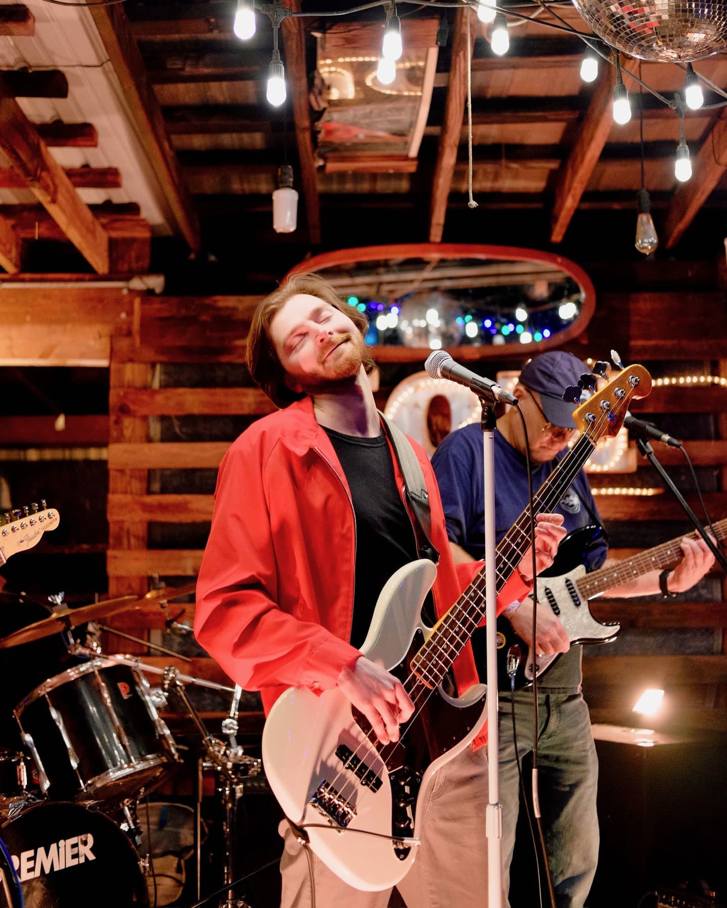 Lee mid-song in a red jacket, playing bass under the string lights
